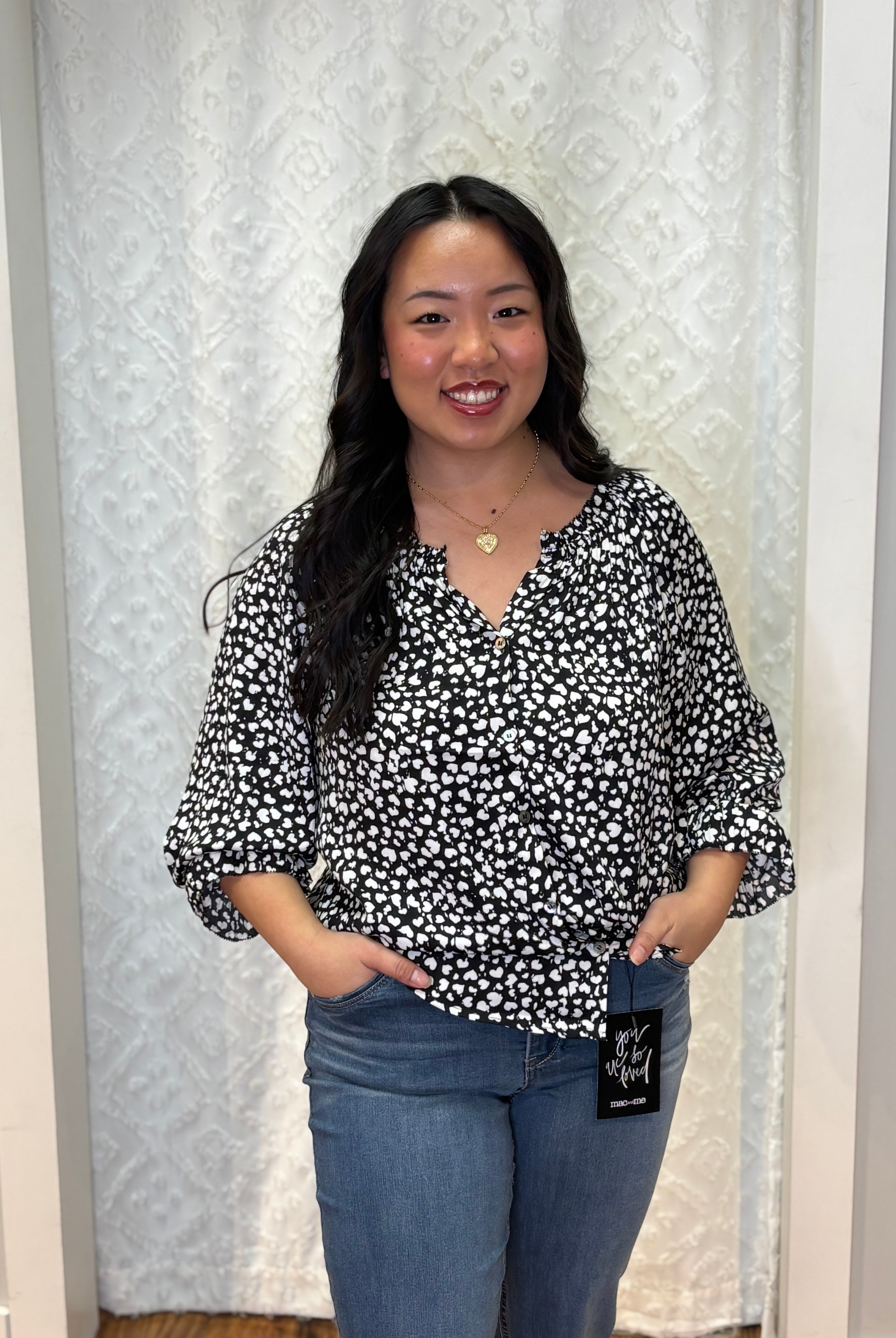 Person wearing black v-neck polyester blouse with small white asymmetrical hearts